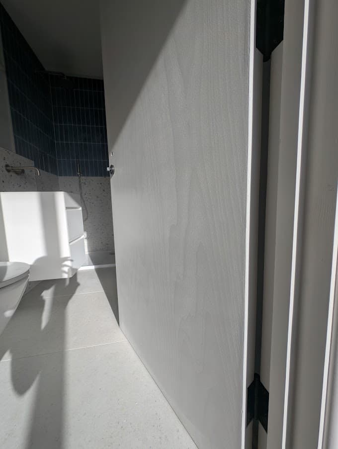 A grey painted wardrobe wall opening onto a bathroom with dark tiled walls, a white vanity unit and a toilet visible beyond