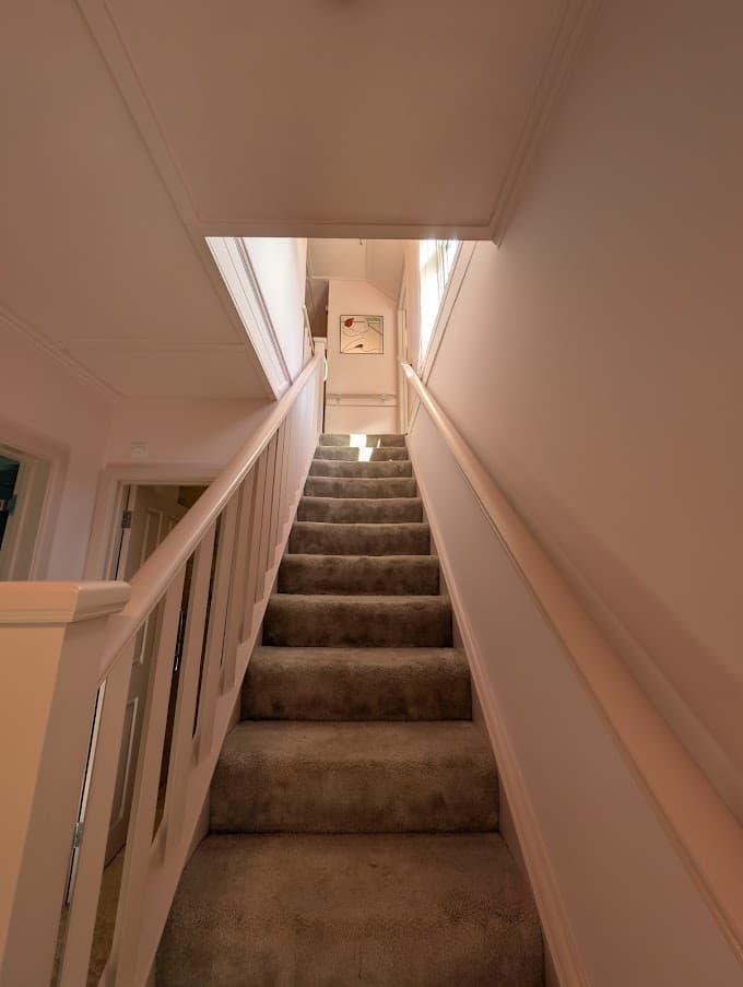 A staircase decorated in a warm neutral tone, with a white painted balustrade and a stair carpet runner