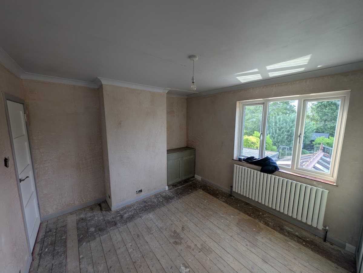 A freshly plastered bedroom mid-preparation, with a mist coat on the walls, a radiator and bare floorboards