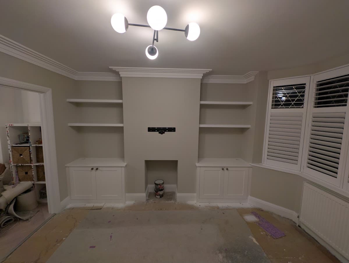 A finished fireplace chimney breast with painted built-in alcove shelving and cabinets on either side