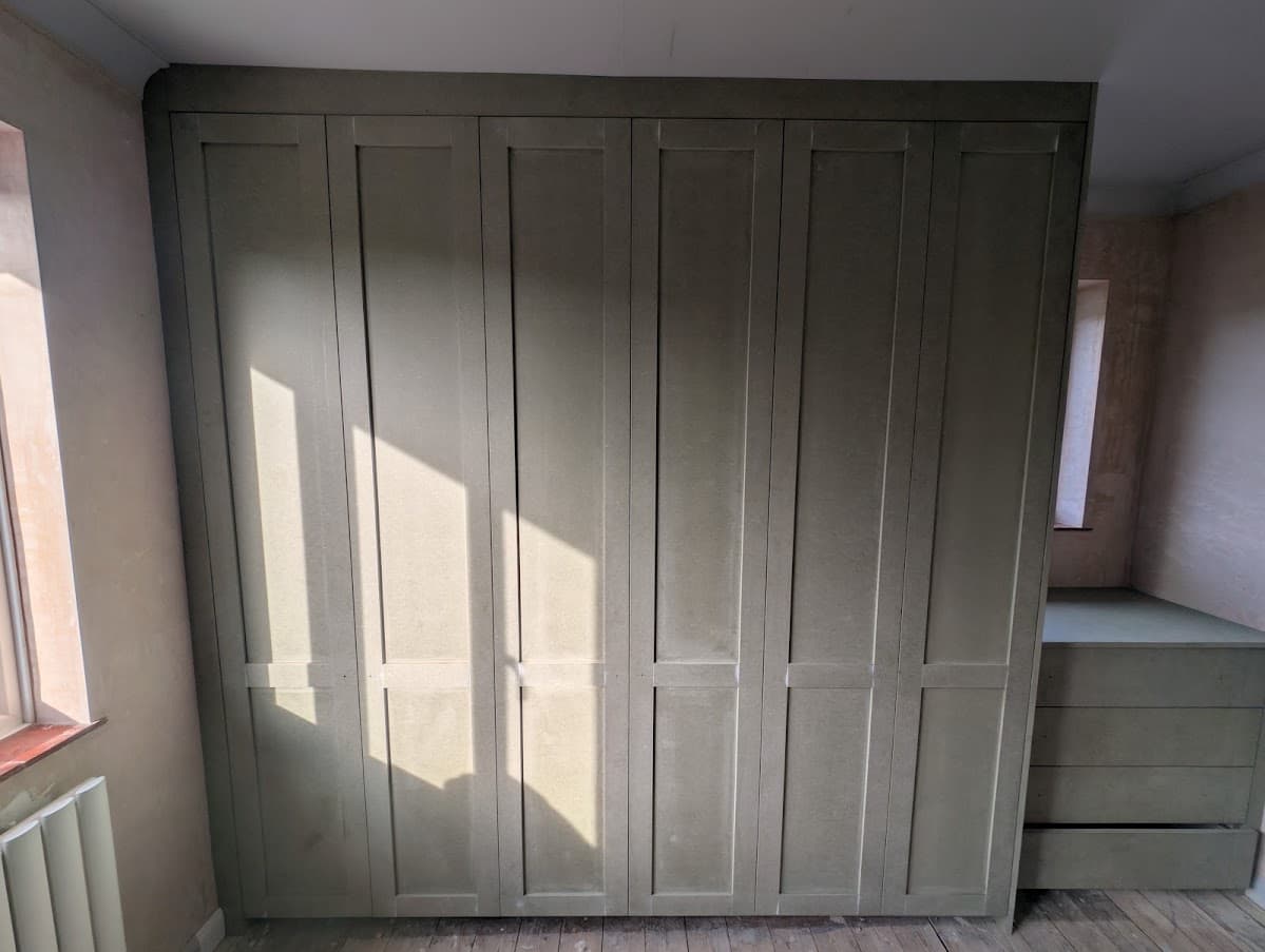 Close view of six sprayed sage green wardrobe doors with shaker-style panel detail