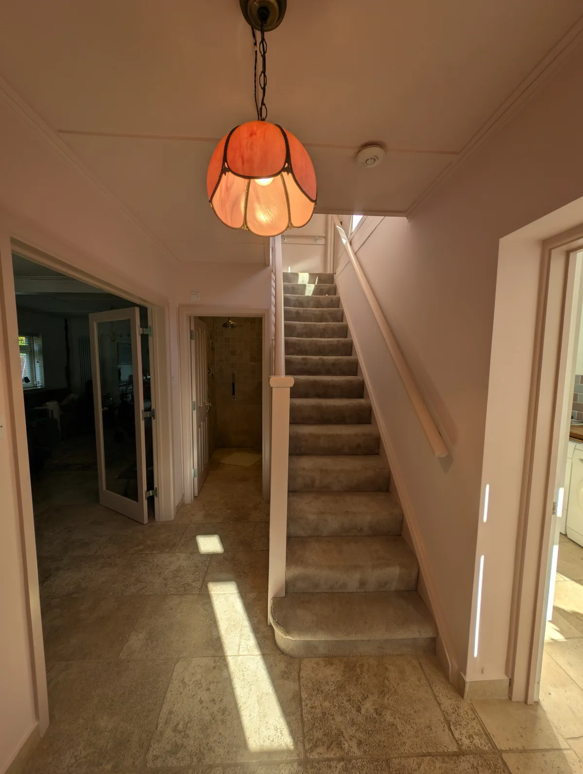 Finished hallway and staircase in a soft pink, with a stained glass pendant light, oak doors and a clean stair runner