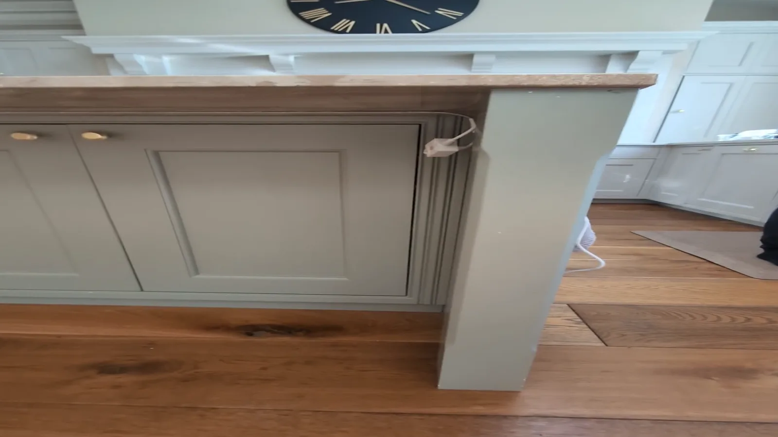 Kitchen island finished in a sprayed sage green, shown alongside matching white cabinetry and an oak floor