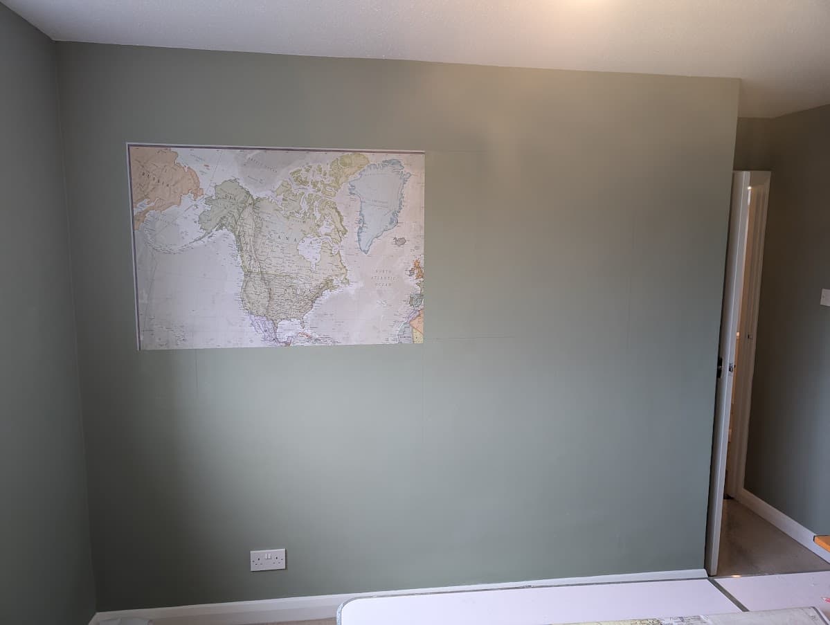 A single panel of a world map wallpaper mural mounted on an olive green wall in an empty room with a doorway to one side
